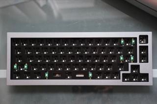 A top-down shot of a grey 65% keyboard with no keycaps or switches.