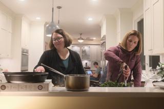 Two women cooking side-by-side at a stove.