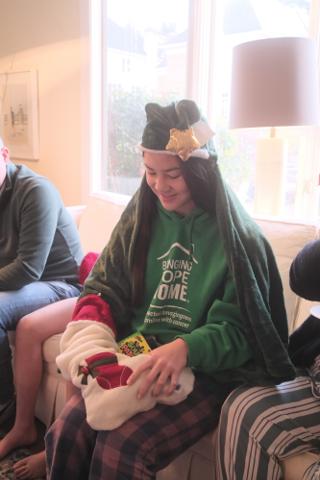 A young woman in a festive hat pulling gifts out of a Christmas stocking.