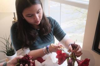 A young woman in a green top trims a flower.