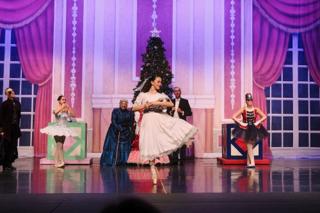 A dancer holding a Nutcracker doll balances en pointe.