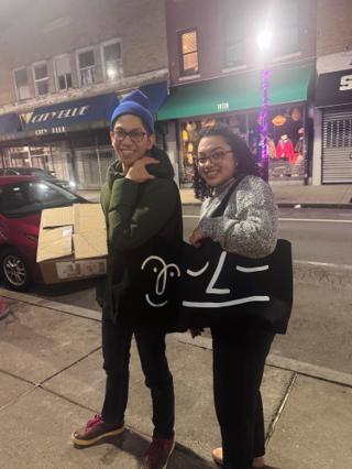 Two people carrying black tote bags with slightly different smiley face logos.