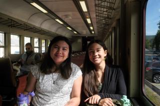 Two young women smile aboard a train car.