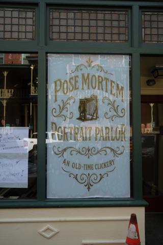 A painted sign on shop glass for Pose Mortem Portrait Parlor, “An Old-Time Clickery”.