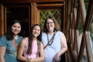 A woman and her two daughters smile by the window of a large treehouse.