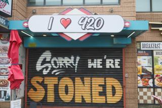 A shop named I heart 420 with a closed iron gate spray painted with "Sorry We’re Stoned".