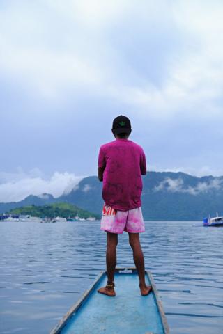 A man stands on the bow of an outrigger boat.