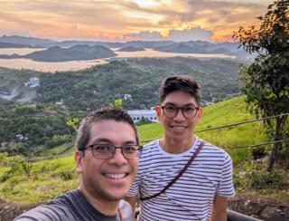 Two men in the foreground of a sunset on an island bay