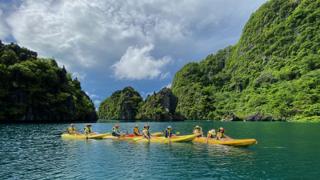 Four kayaks lined up in line with the horizon, with island cliffs in the background.