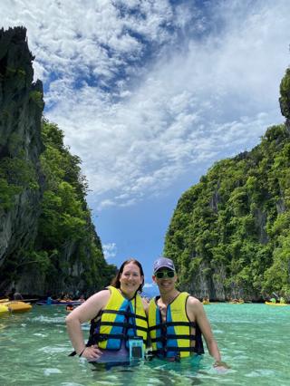 A man and a woman in waist-deep water flanked by two island cliffs in the background.