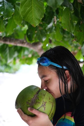 A woman sips from a young coconut.