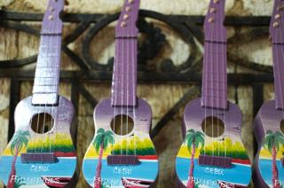 Three purple ukeleles painted with a beach scene hanging in a row.