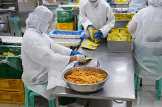 Workers at a bench fill bags with dried mangoes.