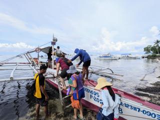 A family boards an outrigger boat using a short set of wooden stairs.