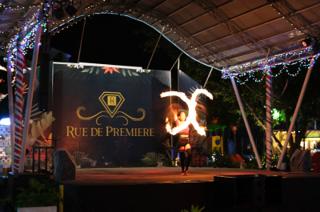 A woman on stage twirls fire, creating two intersecting arcs in front of her.
