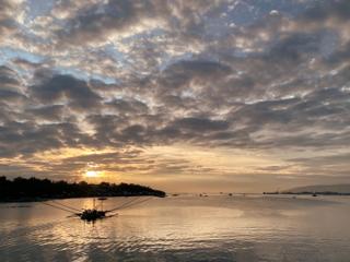 A view into a sunset with outrigger boats silhouetted against the sun.