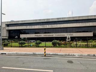 A long, concrete-and-glass building with a metal sign “Philippine International Convention Center” over the entrance.