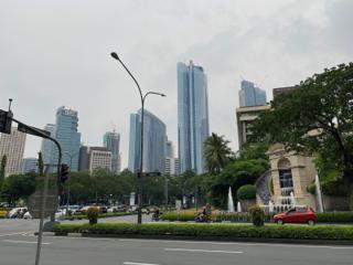 A busy intersection. To the right is a hotel with a fountain surrounded by decorative steps, in the distance are skyscrapers and office buildings.
