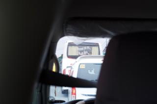 A view of traffic, shot from within a van. Through the windshield a bus is in view, with wavy text stenciled on the rear windshield saying “Wherever you are…We are there…”