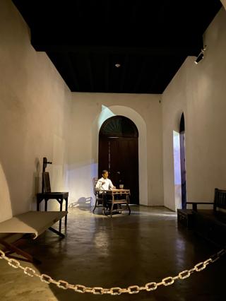 A statue of Jose Rizal at a writing desk. He is dressed in the traditional formal <em>barong Tagalog</em> and holds a pen.