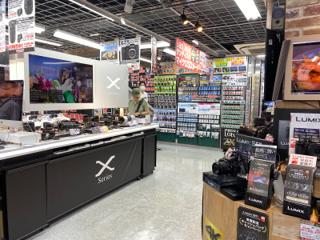 A camera shop display with multiple camera bodies and lenses densely arranged around a table.