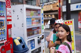 Two girls in front of a row of vending machines.