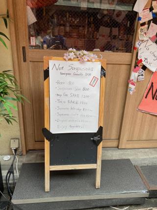 A sign for “Not Suspicious Bar” with a price list for beer, sake, and cocktails.