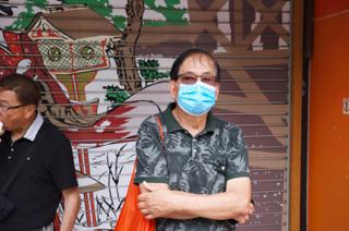 A man in a mask stands in front of a store with a decorative metal sliding door.