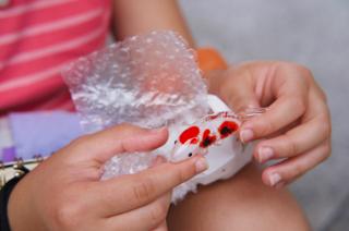 A girl unwraps a delicate glass figurine of a koi.