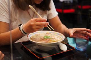 A girl holds chopsticks poised over a bowl of ramen.