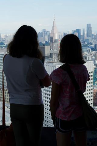 Silhouette of two girls looking out on Tokyo through a floor-to-ceiling window.