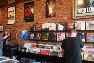 A person browses the racks in a record store. The brick wall is decorated with posters.