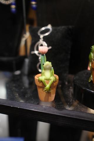 A small plant with a sculpted frog sitting on the edge of the pot.