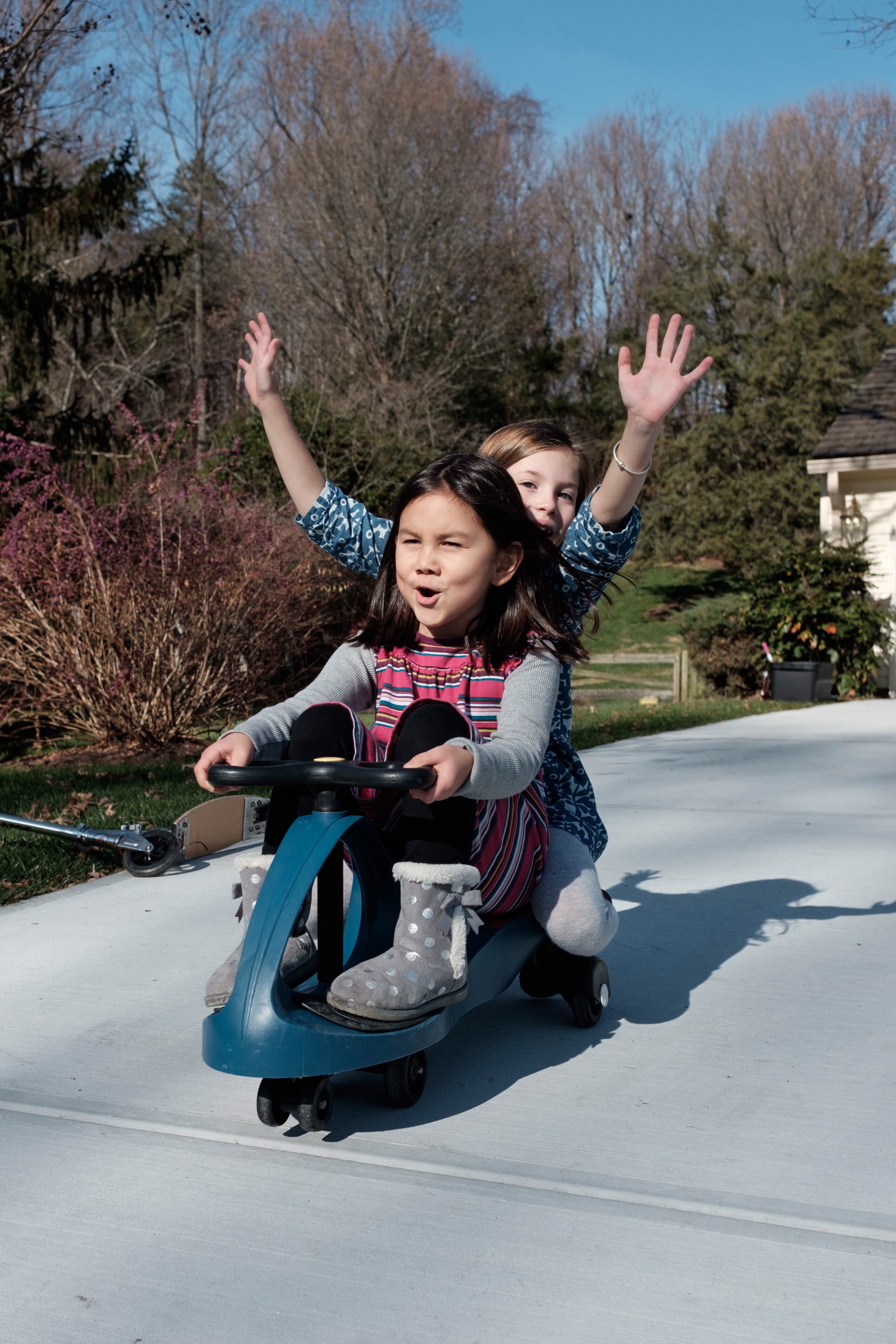 Em in Classic Chrome Two girls on a scooter rolling down a driveway.