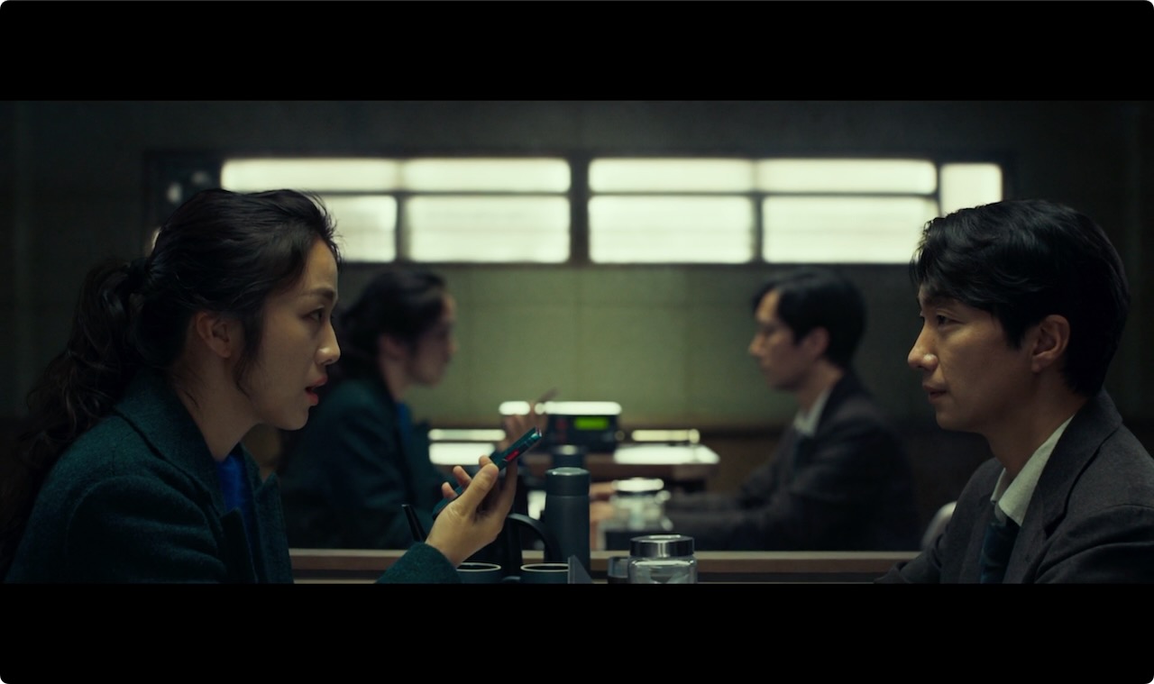 Starting on the same plane. *Image © Mubi* A man and a woman sit facing each other, their reflections visible in a mirror in the near distance.