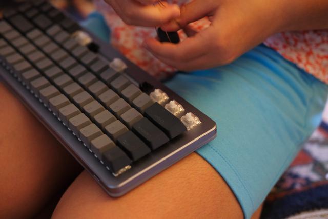 Girl pulls keycaps from a keyboard.