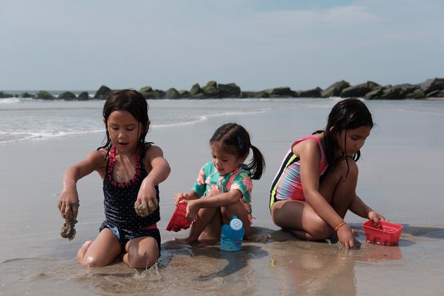 Three girls play in the sand by the water line.