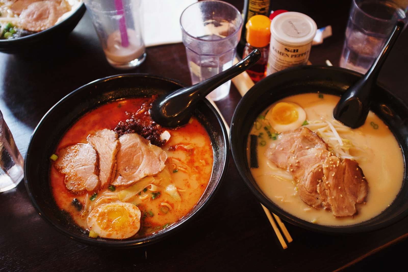 Two bowls of ramen, one of which contains a fiery red spicy broth .”