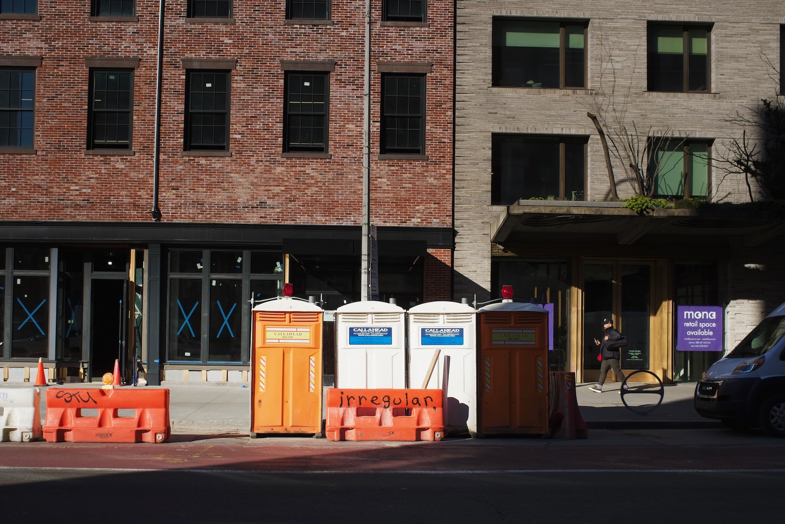 An orange construction barrier with the word “irregular” spray painted on it sits in front of a row of portable toilets.