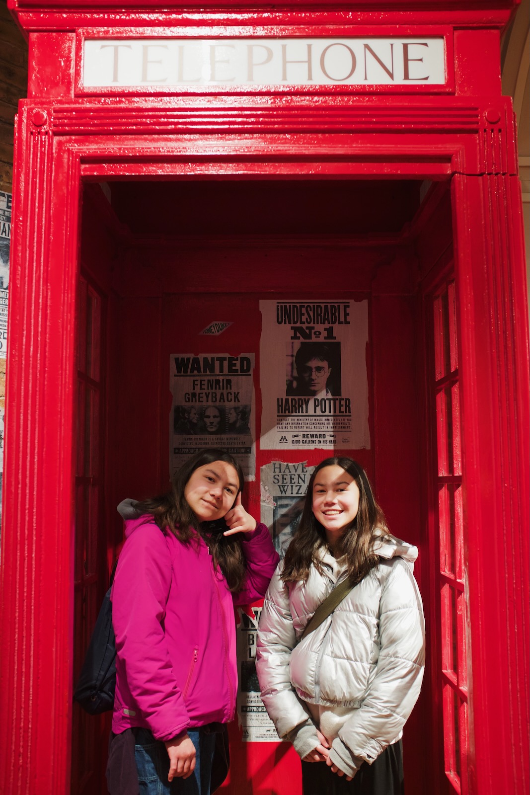 Two girls smile from within a replica London phone booth within the Harry Potter store in New York City.