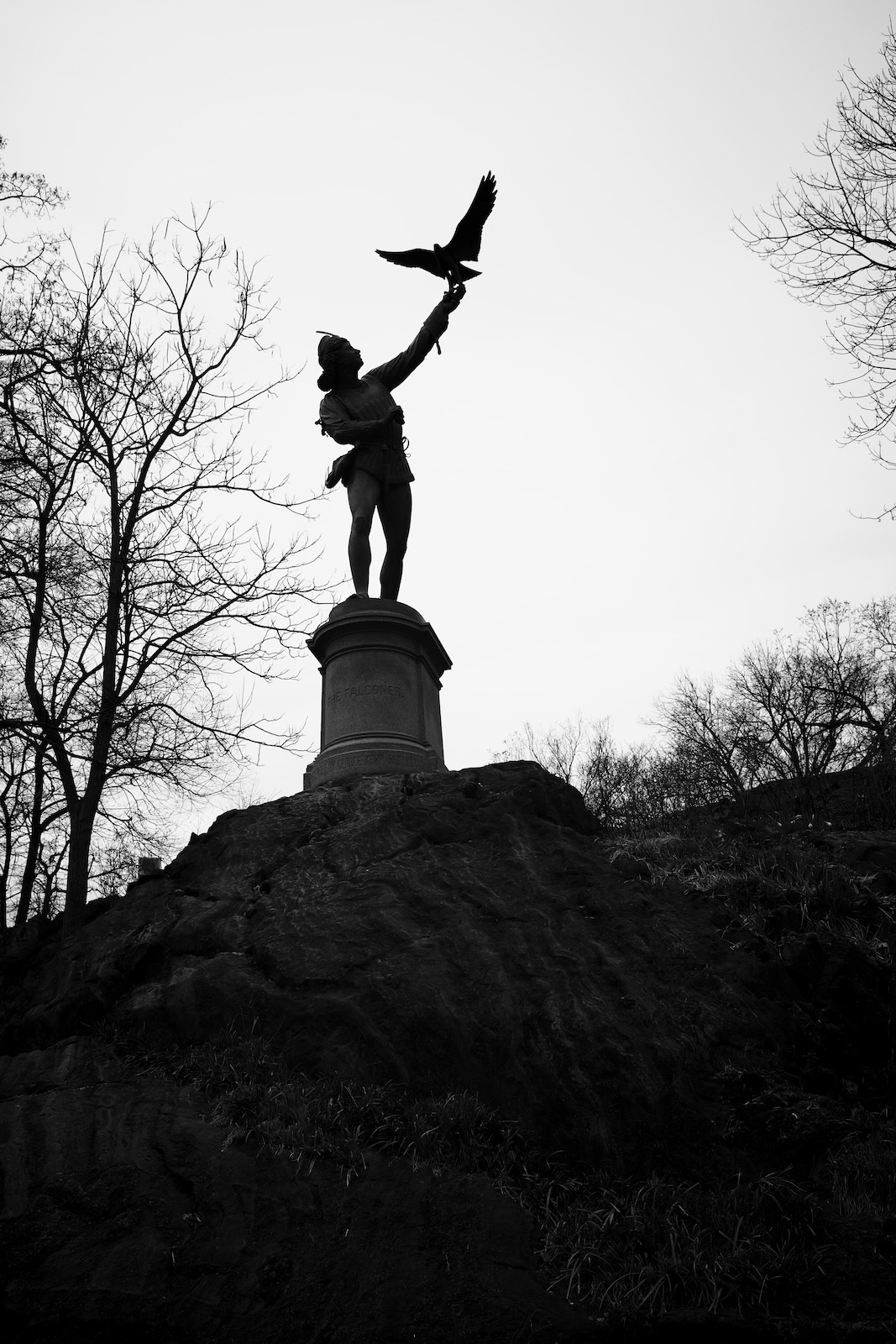The Falconer sculpture in Central Park, silhouetted by the sun. The sculpture features a man extending his arm as a falcon alights on it.”