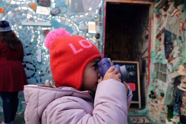 Girl in a knit hat peers through the viewfinder of an instant camera.