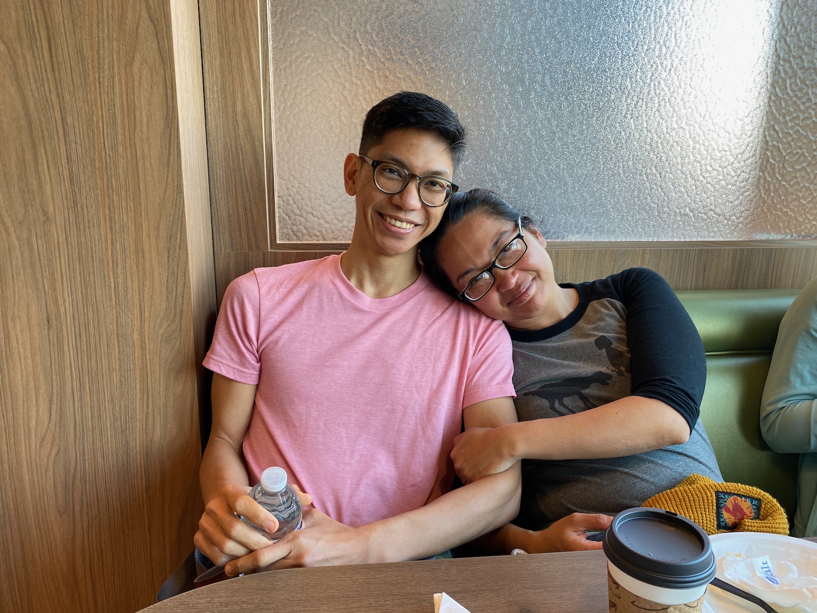 A man and a woman sit in a dining area booth, with the woman resting her head on the man’s shoulder