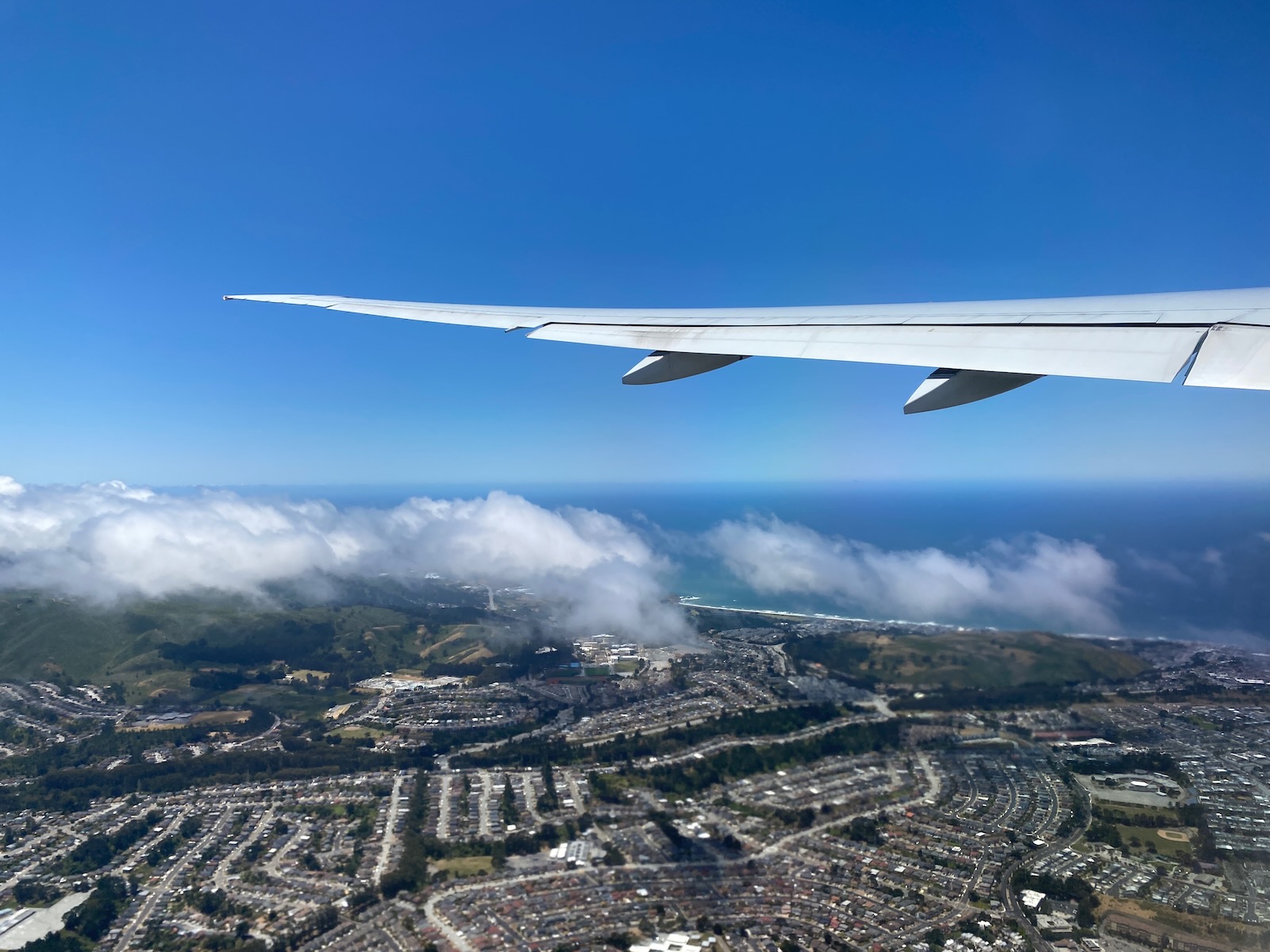 A view of San Francisco from an airplane window, with clouds above the ground and ocean.