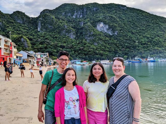 A family photo in front of a beach with a hillside in the background.