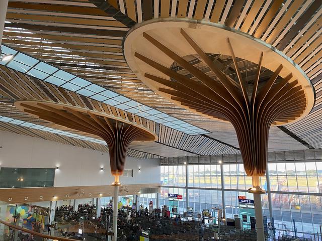 Two pillars with wooden decoration extend to an airport ceiling.