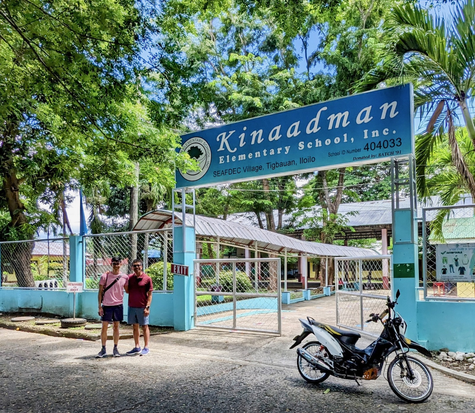 Elementary school. Photo © Joseph Llobrera. Two men stand in front of a gated entrace to an elementary school called Kinaadman.