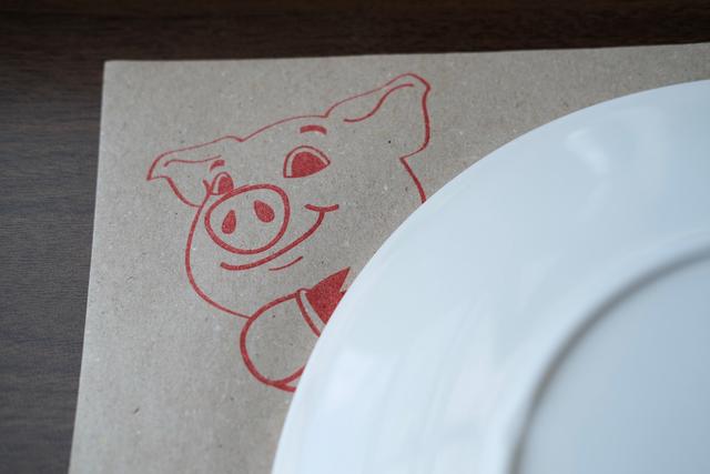 An illustrated pig printed to give the impression of it peeking around a plate.