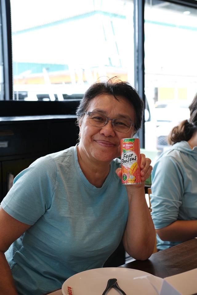 A smiling woman holds up a can of Del Monte Four Seasons fruit juice.