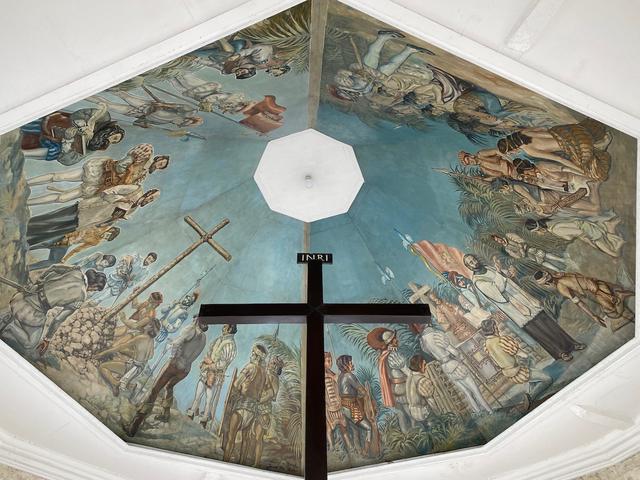 A cross in the center of a room with a painted ceiling marking the events of Magellan’s arrival in the Philippines.